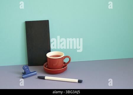 Notebook, pen, clip, cup of tea on purple desk. blue background. workspace Stock Photo