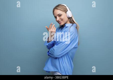 Close-up photo of a charming girl in big wireless headphones on a blue isolated background Stock Photo
