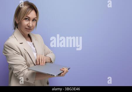 Successful blond young woman in a business jacket with a laptop on a studio background Stock Photo
