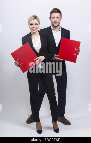 Couple of young caucasian businesswoman with ponytail in black suit and businessman in black suit both hold paper folders, look at camera Isolated on Stock Photo