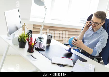 A handsome young man with glasses, blue trousers and a light shirt is working in the office. On the back of the chair hangs his jacket. photo with dep Stock Photo
