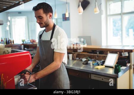 Male barista operating red espresso machine behind wooden counter in coffee shop with knock box Stock Photo