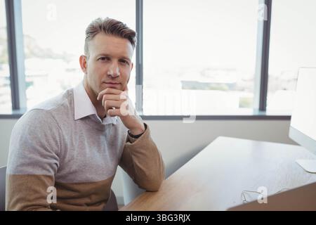 Office worker resting chin on hand at desk by window with computer and keyboard, copy space Stock Photo