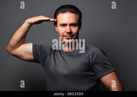 Young strong smiling man showing salute gesture, portrait on gray background Stock Photo