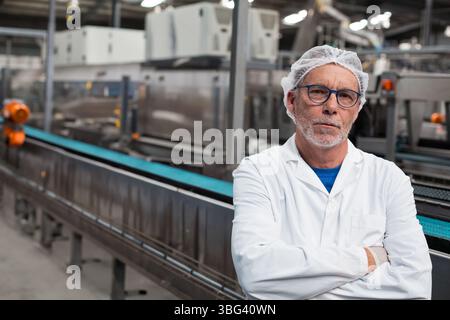 Senior man wearing protective attire inspecting conveyor belt in manufacturing plant, copy space Stock Photo