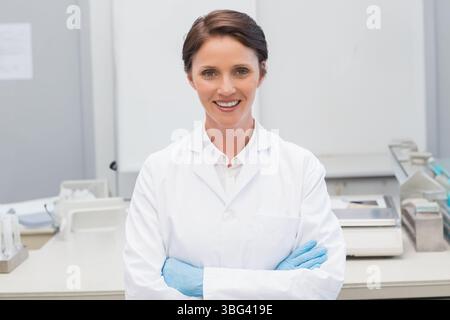 Mid adult woman wearing lab coat and gloves smiling while handling test tubes at laboratory bench Stock Photo