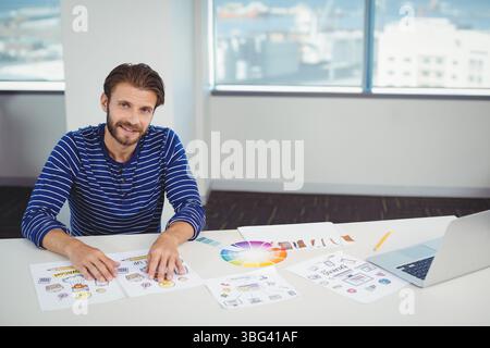 Male designer reviewing mockups with color wheel at office desk with laptop and pencil, copy space Stock Photo