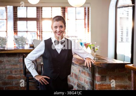 Female bartender wearing uniform serving at brick counter offering colorful cocktails Stock Photo
