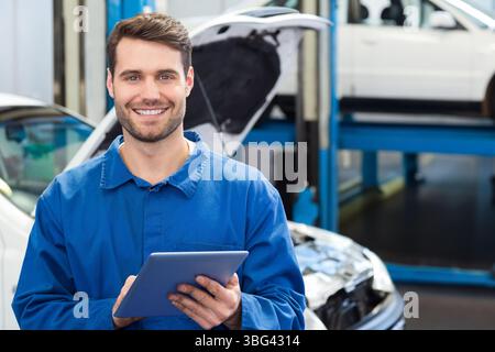 Male auto mechanic standing in workshop holding tablet and inspecting white sedan on hydraulic lift Stock Photo
