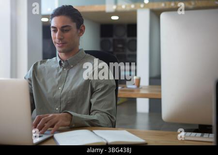 Middle Eastern man typing on laptop with notebook, coffee cup and speakers in office, copy space Stock Photo