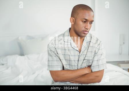 African American man sitting on bed in bedroom under intercom in plaid pajamas, copy space Stock Photo
