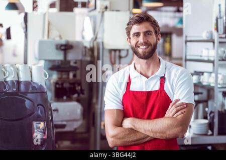 Man in late twenties in red apron, white polo making coffee at cafe using espresso machine Stock Photo