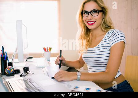 Woman working on digital design in home office wearing striped top with graphics tablet, copy space Stock Photo