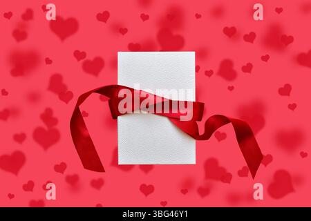 White gift box with red ribbon on red hearts pattern background Stock Photo