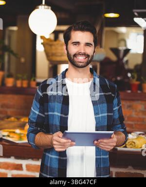 Smiling cafe manager holding tablet in bakery with counter displaying pastries under globe light Stock Photo