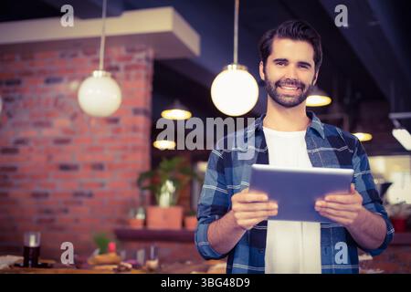 Tablet resting on wooden counter in cozy brick wall cafe, featuring globe lights and pastries Stock Photo