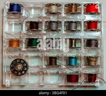 Sewing machine steel bobbins wiht thread in a plastic container Stock Photo