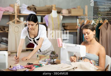 Young seamstresses stitching and drafting paper patterns in workshop Stock Photo