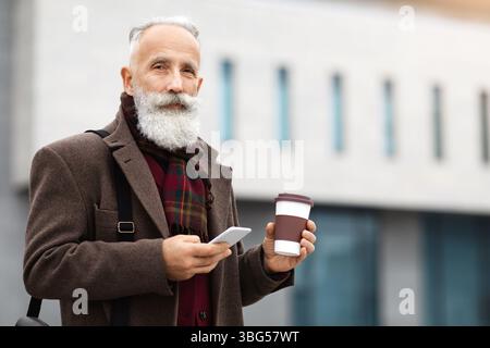 Handsome aged man holding coffee and using smartphone Stock Photo