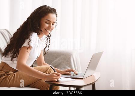 Young lady attending webinar, using laptop and headset Stock Photo