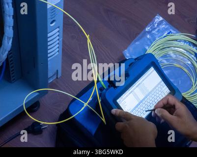 A technician uses fiber optic testing equipment in a workspace, focused on measurements and diagnostics for network performance and connectivity. Stock Photo