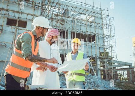 Arab construction engineer architect, Muslim builder working outdoor at construction site with floor plan cooperate with staff worker Stock Photo