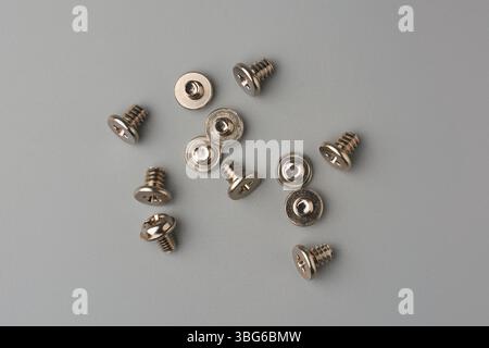 close-up of small silver colored screws scattered on gray textured background surface, machine screws with flat phillips head drive Stock Photo