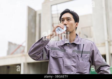 Asian worker male thirsty drinking water in hot summer weather working outdoor at construction site Stock Photo