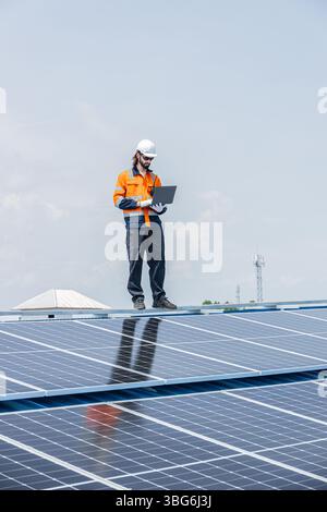 Worker installing solar panels on the roof top using laptop software online monitor checking status of power supply rate Stock Photo