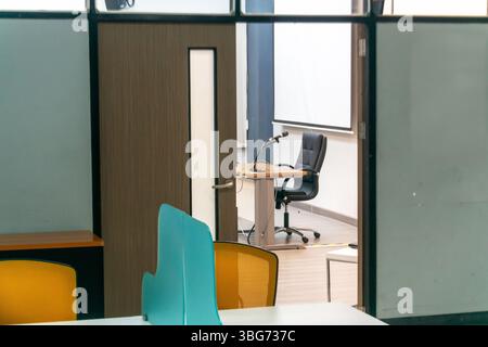A modern office workspace featuring an empty desk and chair with a microphone, viewed through a glass partition, showcasing a professional and organiz Stock Photo