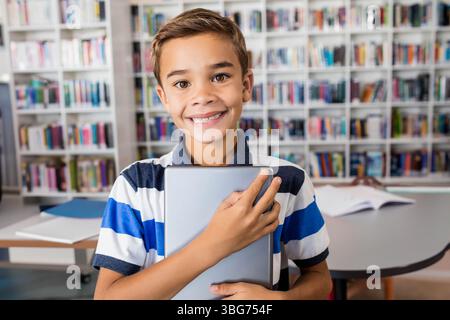 Tablet lying on library table with open notebooks and papers scattered, bookshelves behind Stock Photo