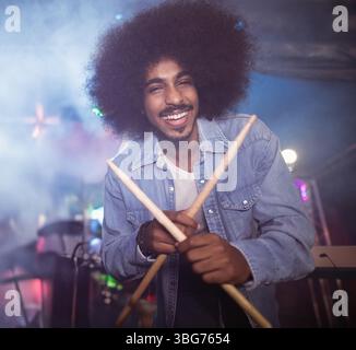 Indian man standing on concert stage holding wooden drumsticks amid colored lights and fog Stock Photo