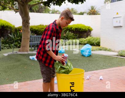 Plastic bottles and green reusable bag being placed into yellow recycling bin on patio Stock Photo
