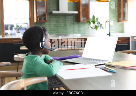 Open laptop displaying blank screen resting on dining table near green backsplash and pencils Stock Photo
