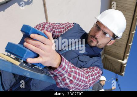 young male builder using electric sander on railing Stock Photo