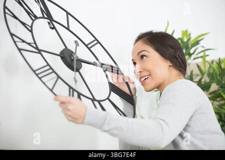 woman hangs a big silver clock on the white wall Stock Photo