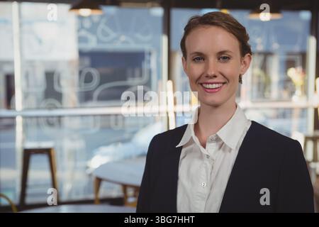 Businesswoman wearing blazer standing in cafe by table and stool under pendant lights, copy space Stock Photo