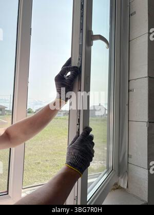 A worker adjusts a plastic window in a new country house. Installing plastic windows in a new building. Construction and renovation concept. Stock Photo