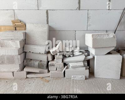 The remains of white building blocks are stacked against a wall at a construction site. Disposal of construction waste. Stock Photo