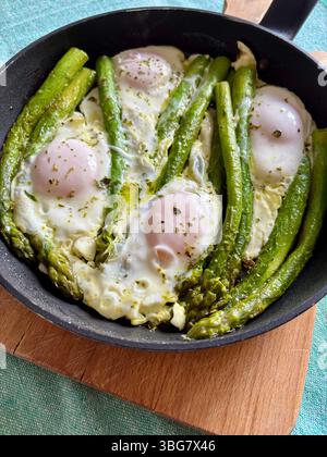 Fried eggs with green asparagus and sprinkled with aromatic herbs in a frying pan. Healthy food. Breakfast concept. Directly above. Stock Photo