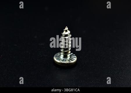 A short self-tapping screw with slots for a Phillips screwdriver lies on a black background. Stock Photo
