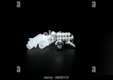 Screws with dowels for fastening parts to the wall lie on a black background. Stock Photo