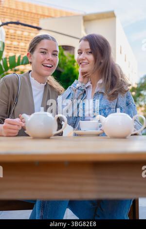 Caucasian women smiling at camera while enjoying tea at outdoor cafe together Stock Photo