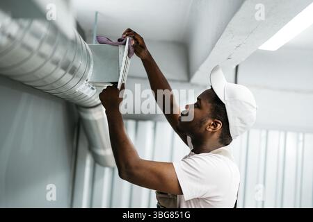 Worker performs maintenance on ventilation system in commercial building during daylight hours Stock Photo