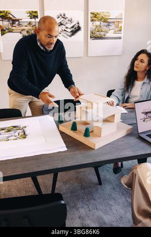 Professionals in a modern office environment collaboratively discuss architectural designs and construction plans using a scale model and printed mate Stock Photo