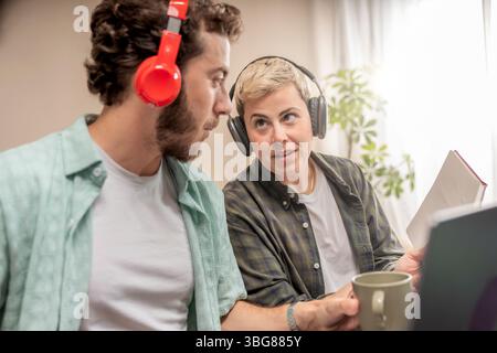 Focused young man and woman wearing headphones, engaged in a collaborative discussion or e-learning session in a bright, modern home office or co-work Stock Photo