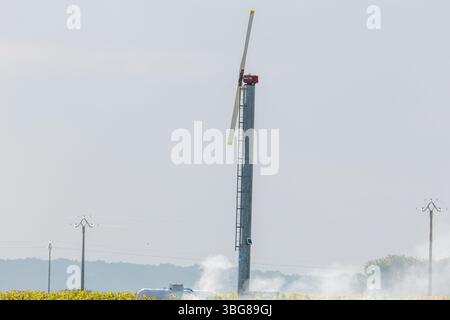 Windmill waterpump Mesland, France - 23.5.2025: A wind turbine with a single blade stands in a field, surrounded by smoke and power lines. Stock Photo