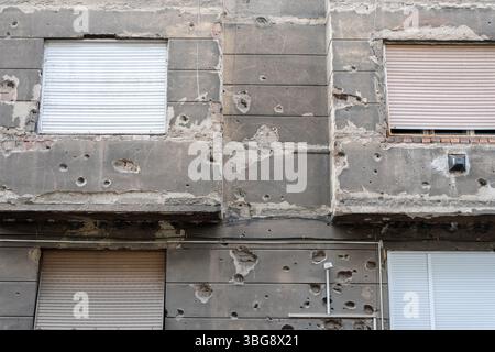 The façade of an old building, mottled with numerous bullet and shrapnel marks, testifying to the military conflict. The closed shutters on the window Stock Photo