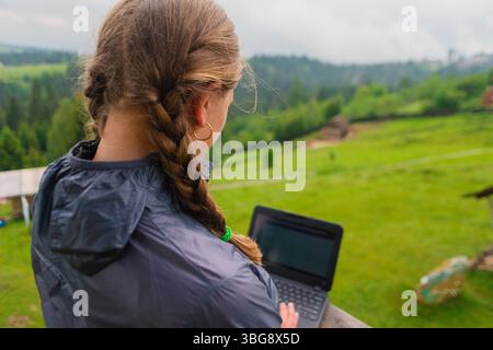 Woman digital nomad working on a laptop at a mountain resort outdoors with a nature background Carpathian Mountains Stock Photo