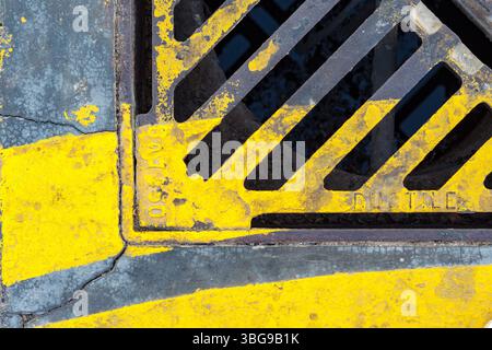 A weathered yellow and gray drainage grate, showcasing the texture and rust of urban infrastructure in Dubai. Stock Photo